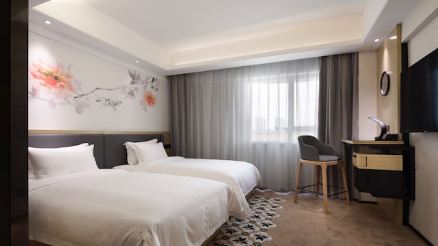 Ein Hotelzimmer mit zwei Betten, einem Schreibtisch, einem Stuhl, einem Fernseher und einer Wanddekoration.