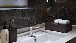 Ein modernes Badezimmer mit einem weißen Waschbecken, dunklen Marmorwänden und einem dekorativen Blumenbild.