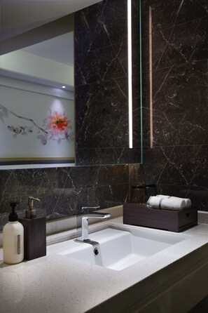 Une salle de bain moderne avec un lavabo blanc, des murs en marbre foncé et un tableau décoratif représentant des fleurs.