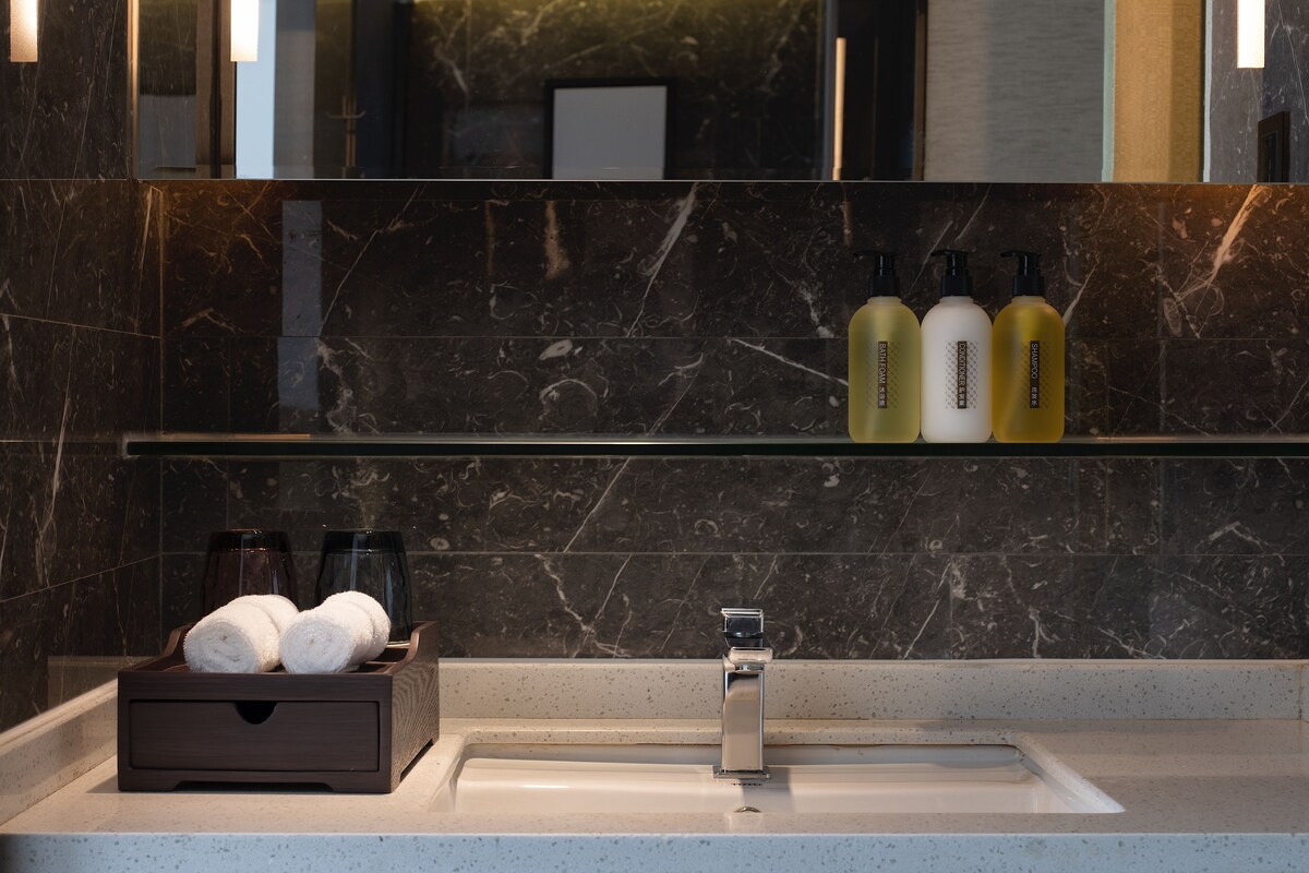 Une salle de bain moderne avec un lavabo en marbre, un miroir et des articles de toilette rangés sur une étagère.