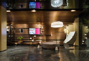 A modern lobby with a wooden slat wall, a round seating area, and a flat-screen TV. - Paco Hotel Jiangtai Lu Metro Guangzhou (Guangzhou)