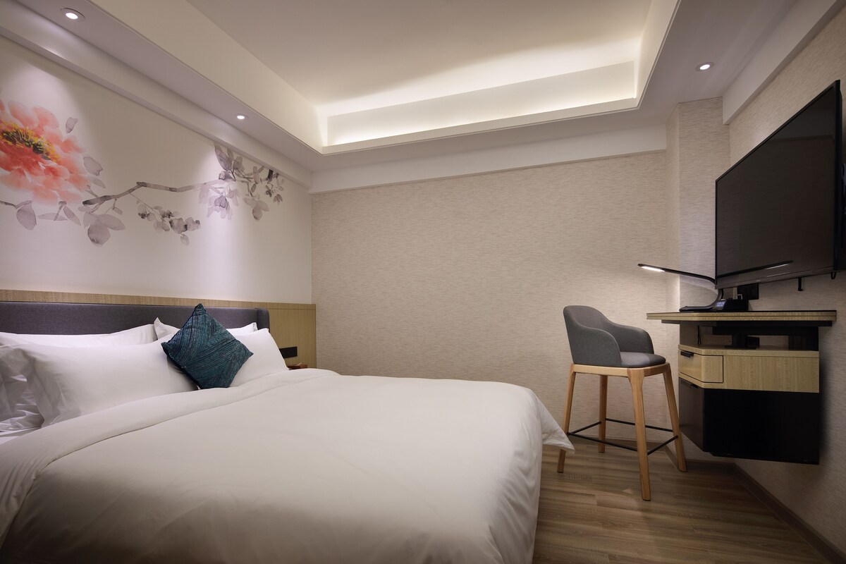 Ein Hotelzimmer mit einem Bett, einem Schreibtisch mit Stuhl, einem Flachbildfernseher und einer Wand mit floralem Wandbild.