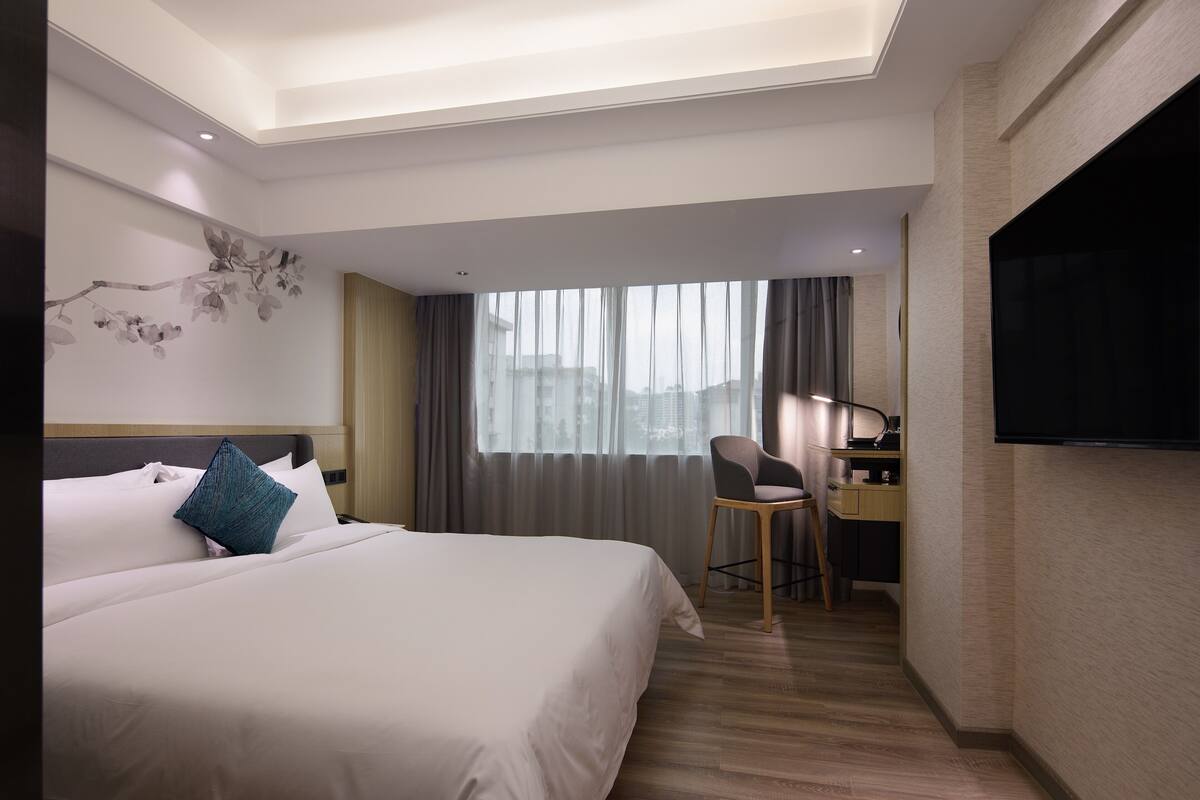 Une chambre d’hôtel avec un grand lit, un bureau avec une chaise, un téléviseur à écran plat et une fenêtre avec des rideaux.