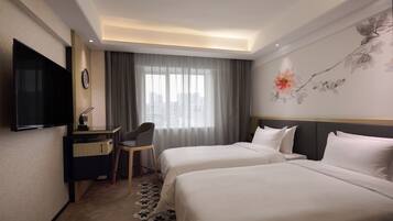Quarto de hotel com duas camas, uma escrivaninha com cadeira, televisão de tela plana e uma janela grande com cortinas.