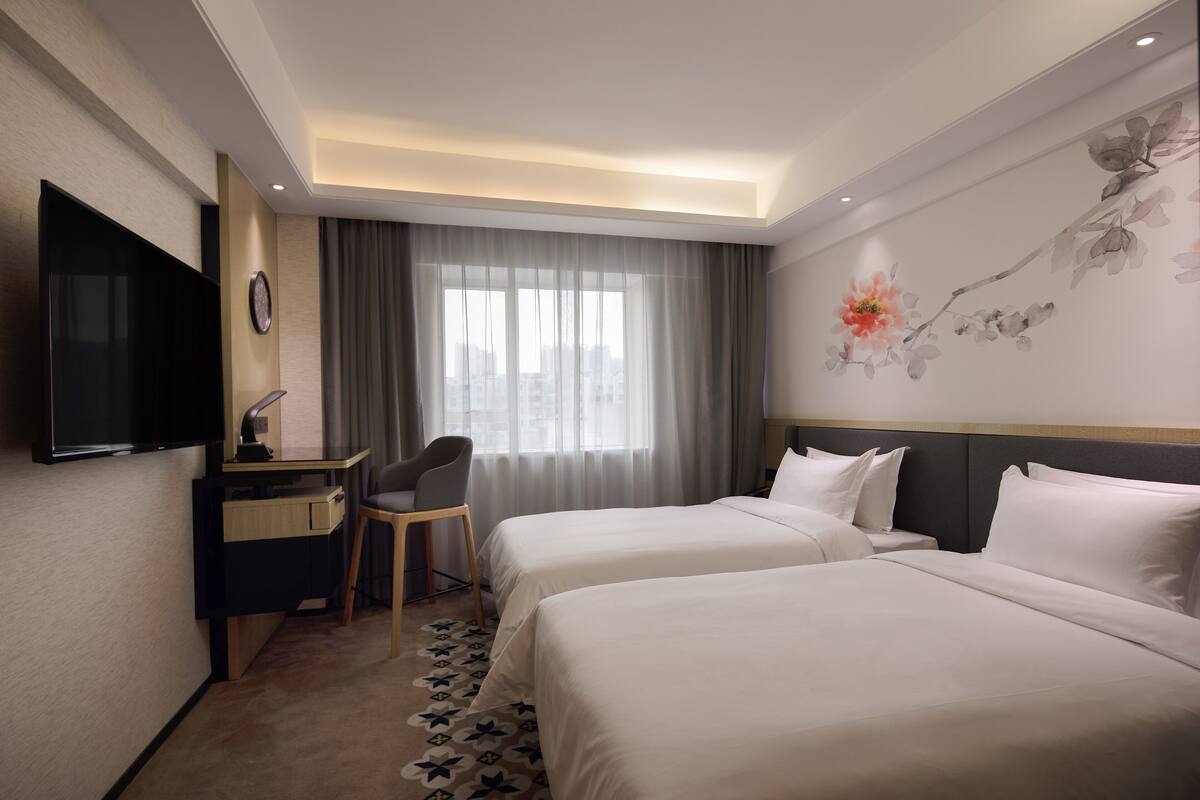 Une chambre d’hôtel avec deux lits, un bureau avec une chaise, un téléviseur à écran plat et une grande fenêtre avec des rideaux.