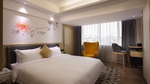 Ein Hotelzimmer mit einem großen Bett, einem Schreibtisch, einem Stuhl und einem Fenster mit Vorhängen.