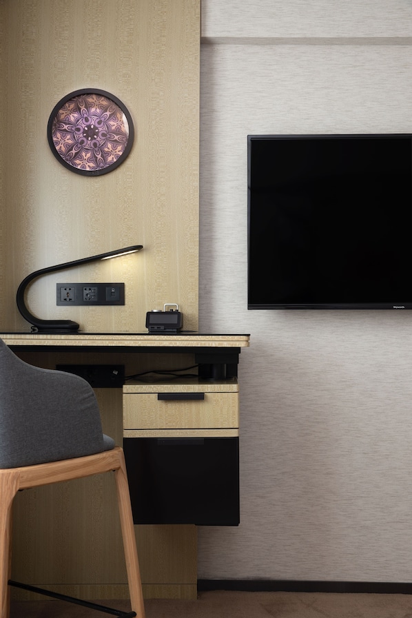 A modern office space with a desk, chair, lamp, and a mounted flat-screen TV. - Paco Hotel Jiangtai Lu Metro Guangzhou (Guangzhou)