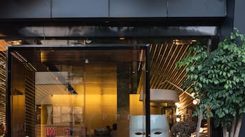 Entrada de um edifício moderno com portas de vidro, uma grande planta em vaso e um lustre decorativo no teto.