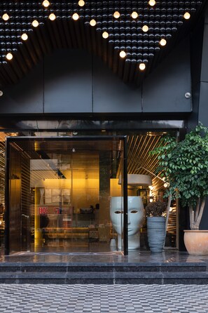 A modern building entrance with glass doors, a large potted plant, and a decorative ceiling light fixture. - Paco Hotel Jiangtai Lu Metro Guangzhou (Guangzhou)