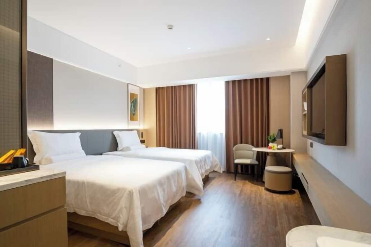 A hotel room with two beds, a desk, a chair, a small table, and a TV mounted on the wall.