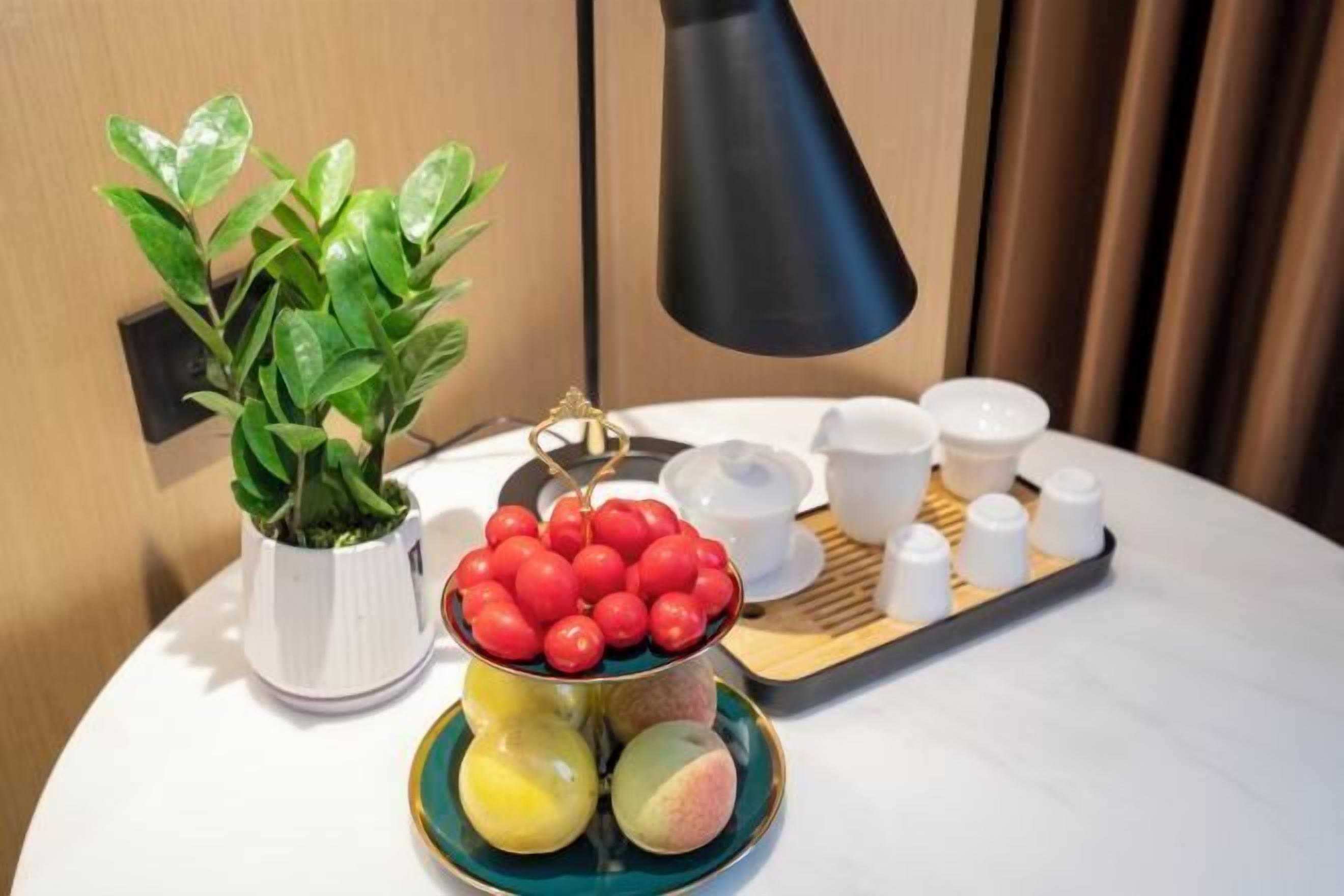 A table with a potted plant, a tray with fruits and condiments, and a black lamp.