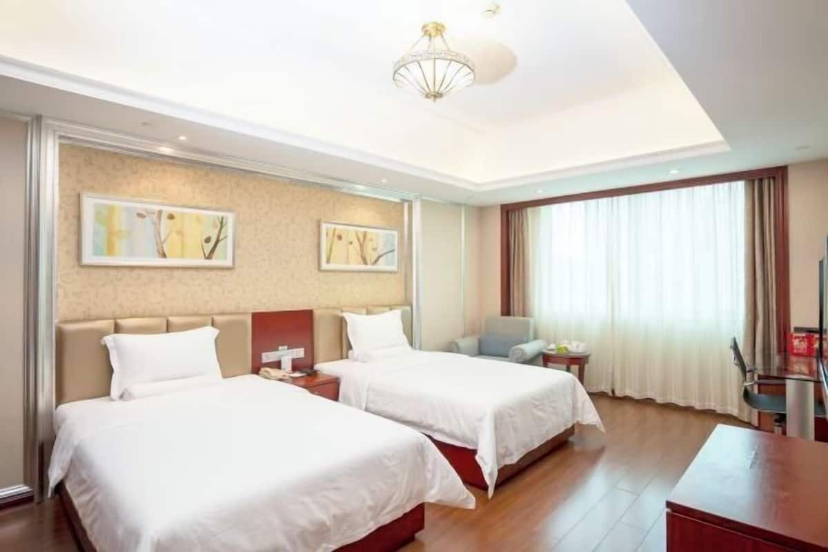 A hotel room with two beds, a desk, a chair, and a large window with curtains.