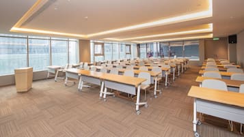 A modern conference room with rows of desks, large windows, and a podium.