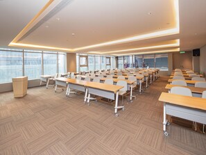 Uma sala de conferência moderna com fileiras de mesas, janelas amplas e um palanque.