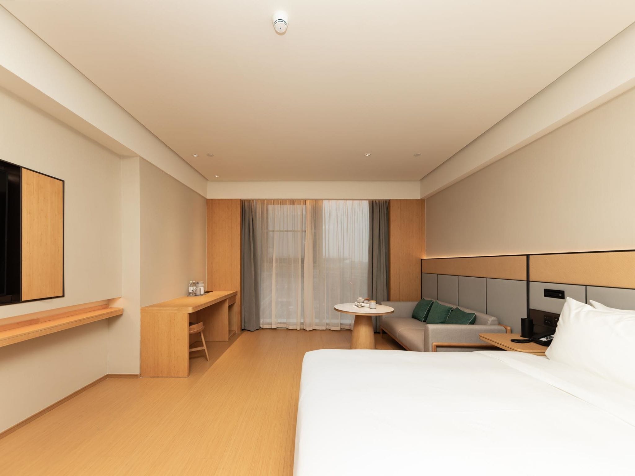 A modern hotel room with a bed, a desk, a chair, a small table, and a TV.