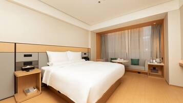 A hotel room with a large bed, bedside tables, a seating area with a table, and a window with curtains.
