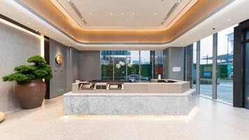 A reception desk with a modern design, a large potted plant, and a view of the outside through large windows.