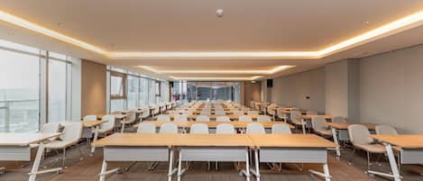Un salón de conferencias con filas de mesas y sillas, ventanas amplias y un diseño moderno del techo.