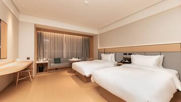A hotel room with two beds, a desk, a sofa, and a large window with curtains.