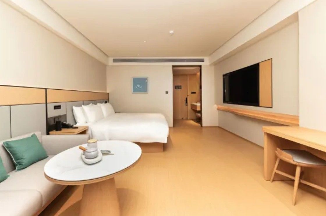 Quarto de hotel com cama, sofá, mesinha, televisão e escrivaninha.
