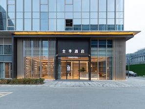 A modern hotel with a glass facade, a sign reading 'JIHOTEL,' and a visible entrance.