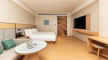 Ein Hotelzimmer mit Bett, Schreibtisch, Fernseher, Couchtisch und Sofa.
