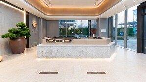 A reception desk with a modern design, a large potted plant, and a view of the outside through large windows. - Ji Hotel Nanjing South Railway Station Square (Nanjing)