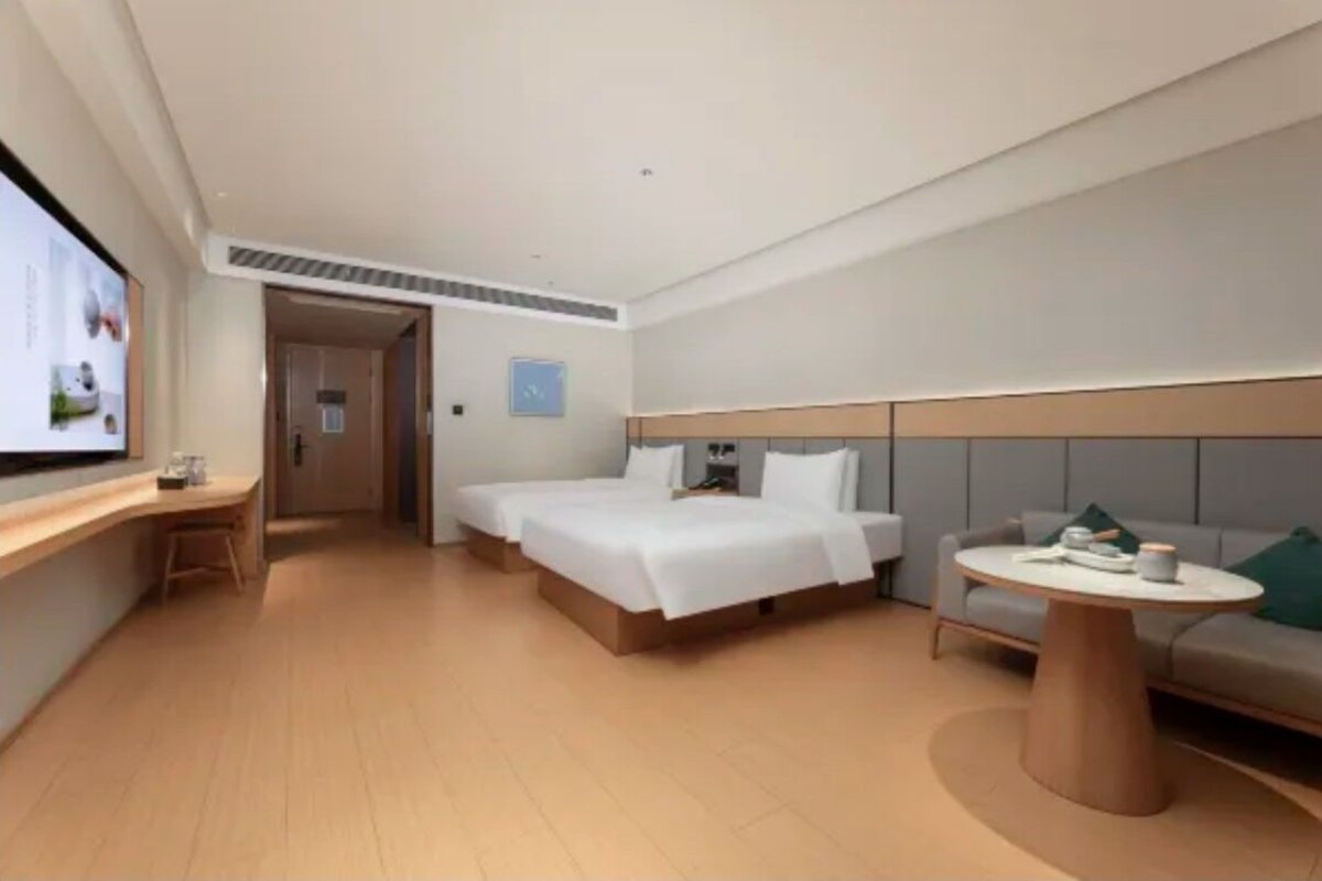A modern hotel room with a bed, a desk, a sofa, and a TV.