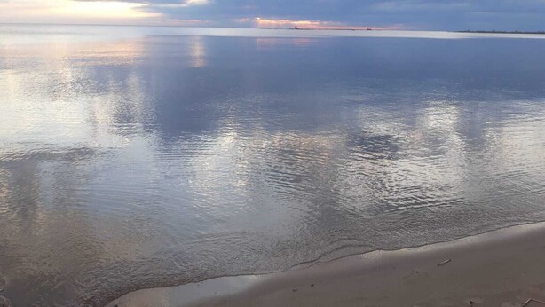 A calm beach with a clear horizon and a distant shoreline.