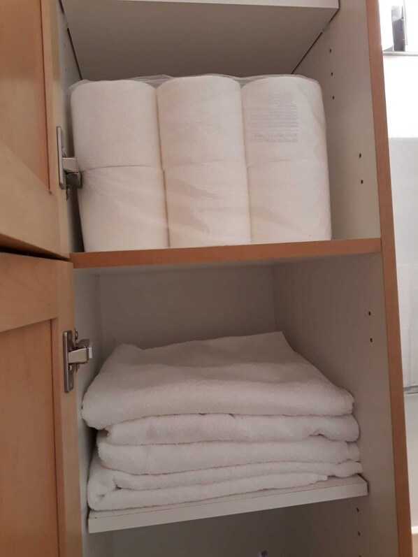 Un armario de madera con dos estantes, cada uno con toallas blancas dobladas cuidadosamente.