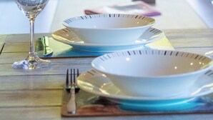 A table set with plates, a glass, and cutlery, with a view of a wooden deck and outdoor furniture in the background. - Spa Pool, Sea and Stunning Views | Cass Bay Escape (Cass Bay)