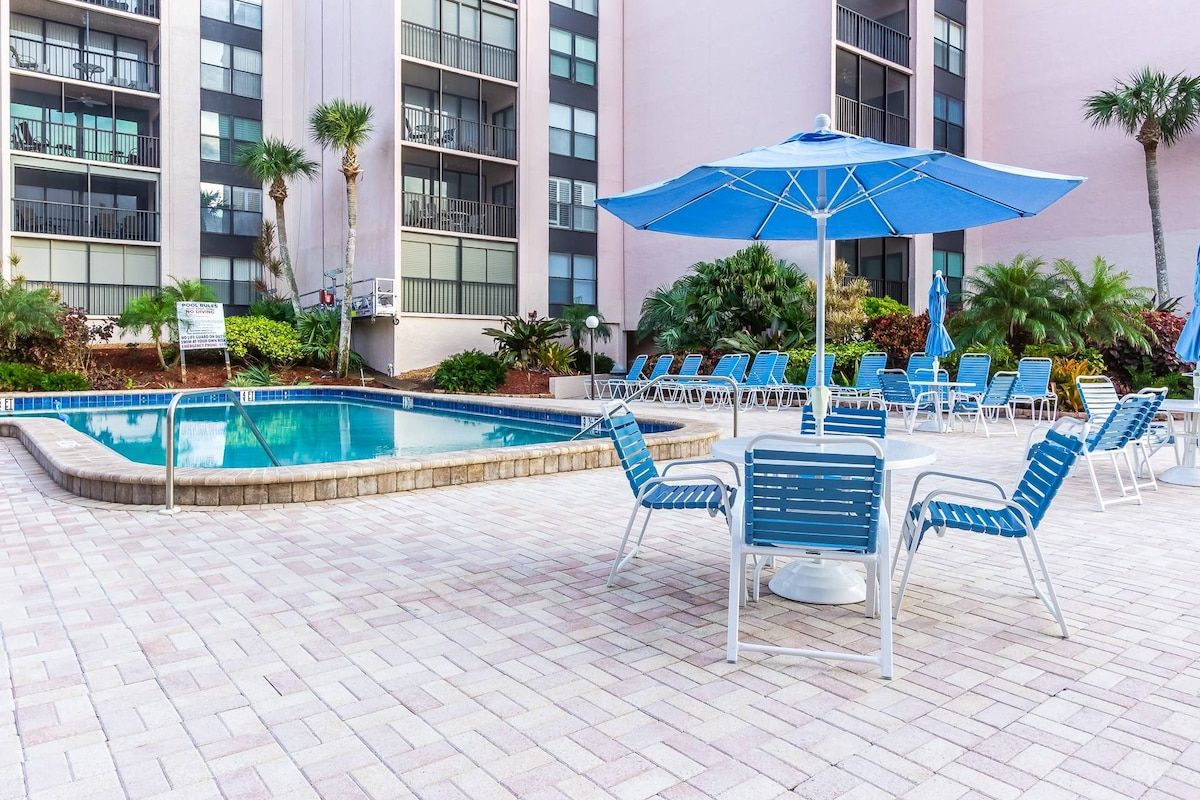 A poolside area with lounge chairs and umbrellas, surrounded by a building with multiple balconies.