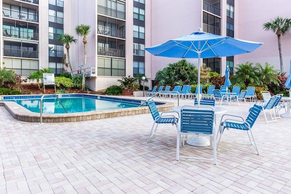 A poolside area with lounge chairs and umbrellas, surrounded by a building with multiple balconies.