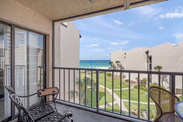 A balcony with a view of the beach, a chair, and a table.
