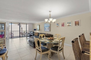 A spacious living area with a dining table, chairs, and a balcony.