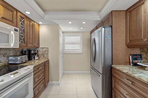 A kitchen with wooden cabinets, a stainless steel refrigerator, a microwave, a stove, and a toaster. - Ocean Views, Private Beach, Pool, Resort amenities (Sarasota)