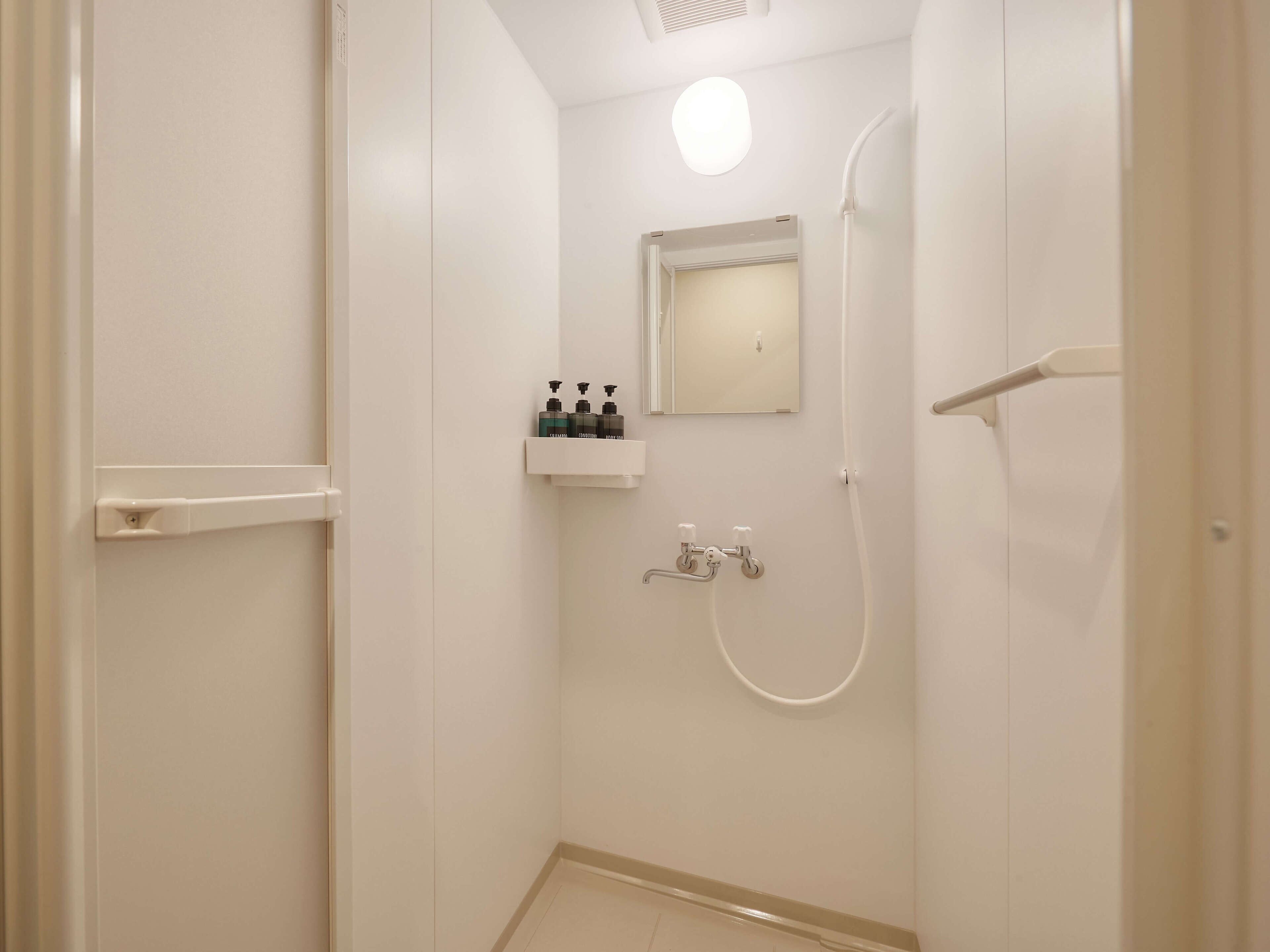 Un baño pequeño y blanco con ducha, espejo y repisa con artículos de aseo.