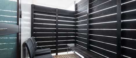 A corner room with a wooden floor, a chair, a small table, and a wall with horizontal light strips.