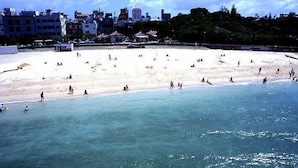 A beach with people sunbathing and swimming, buildings in the background, and a clear sky. - CABIN&HOTEL CONSTANT NAHA (Naha)
