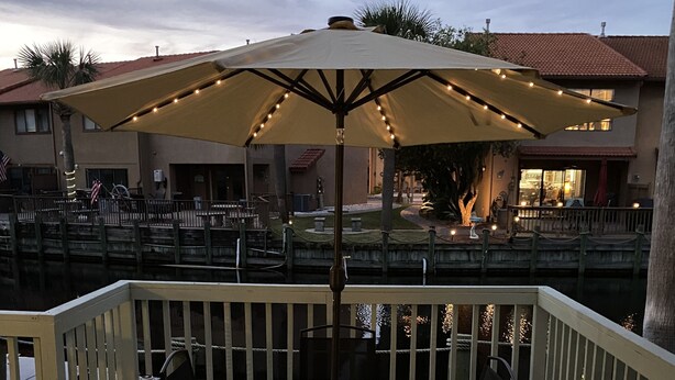 An outdoor patio with a table and chairs under a large umbrella, surrounded by a wooden deck and railing.
