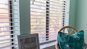 A cozy room with a framed inspirational quote, a wooden chair, a teal pillow, and a small round table with decorative items.