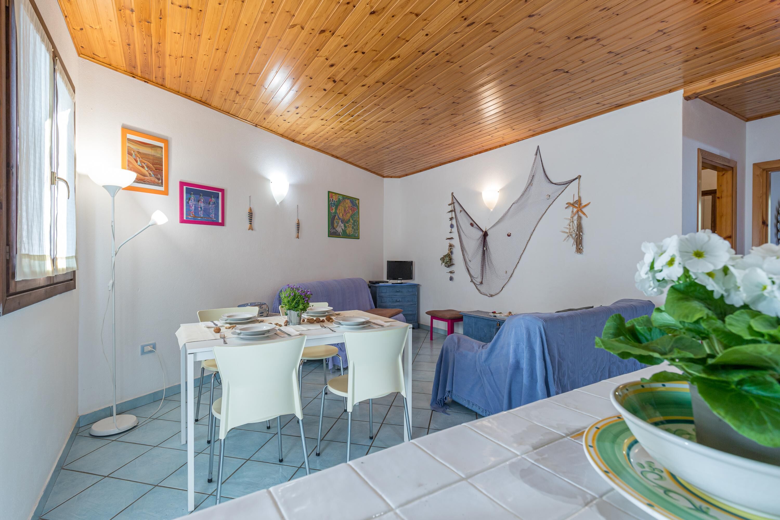 Un comedor con una mesa dispuesta para cuatro personas, un sofá y una pared decorativa con objetos colgantes.