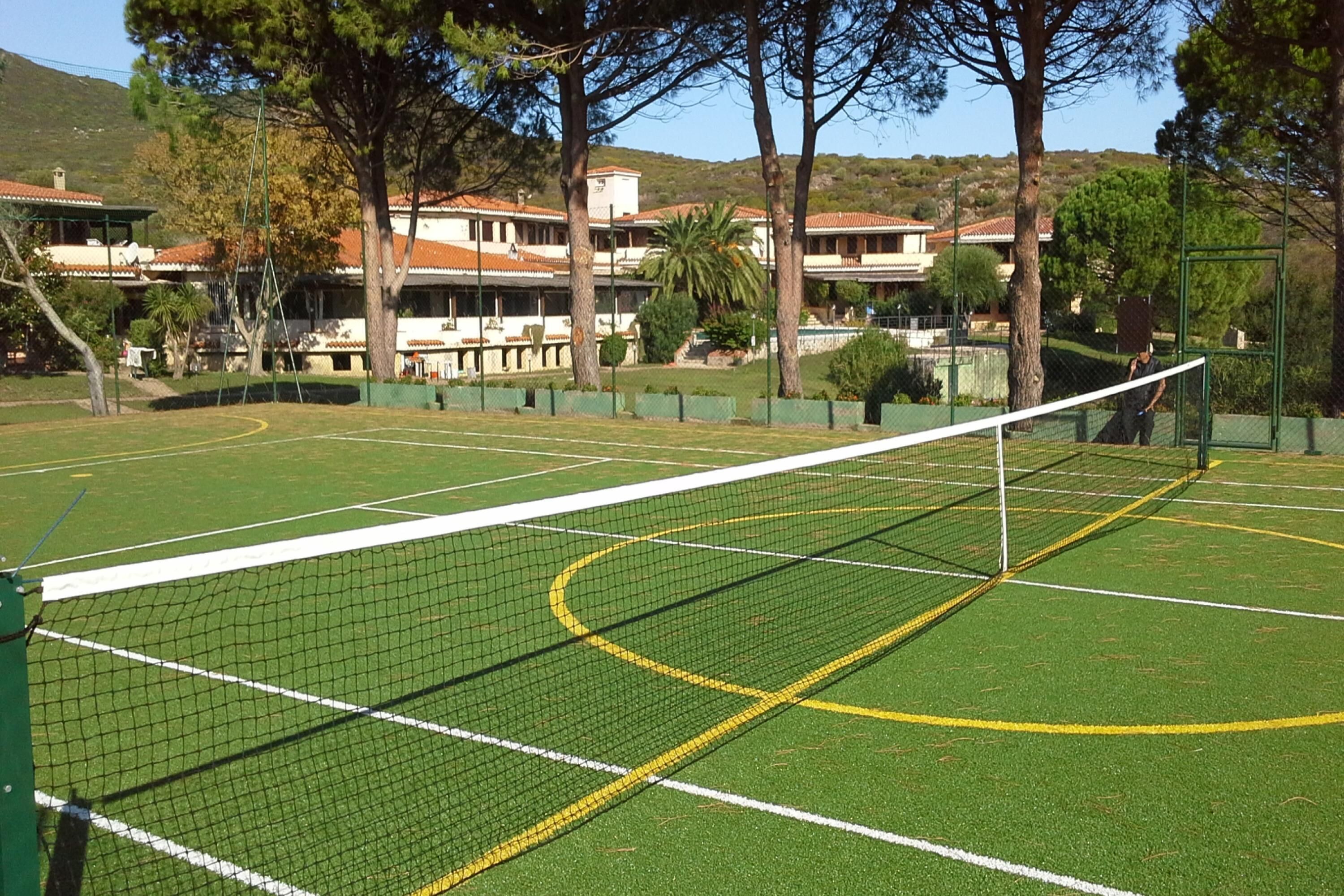 A tennis court with a net, surrounded by trees and buildings.