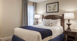 A neatly made bed with a blue and white bedspread, two bedside lamps, and a framed picture on the wall.