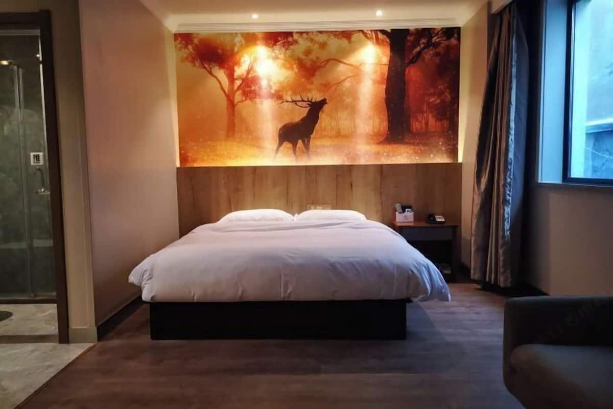 A bedroom with a large bed, a wall-mounted painting of a deer, and a window with curtains.