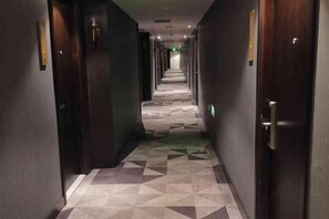 A hotel corridor with patterned flooring, dark walls, and doors with light switches.