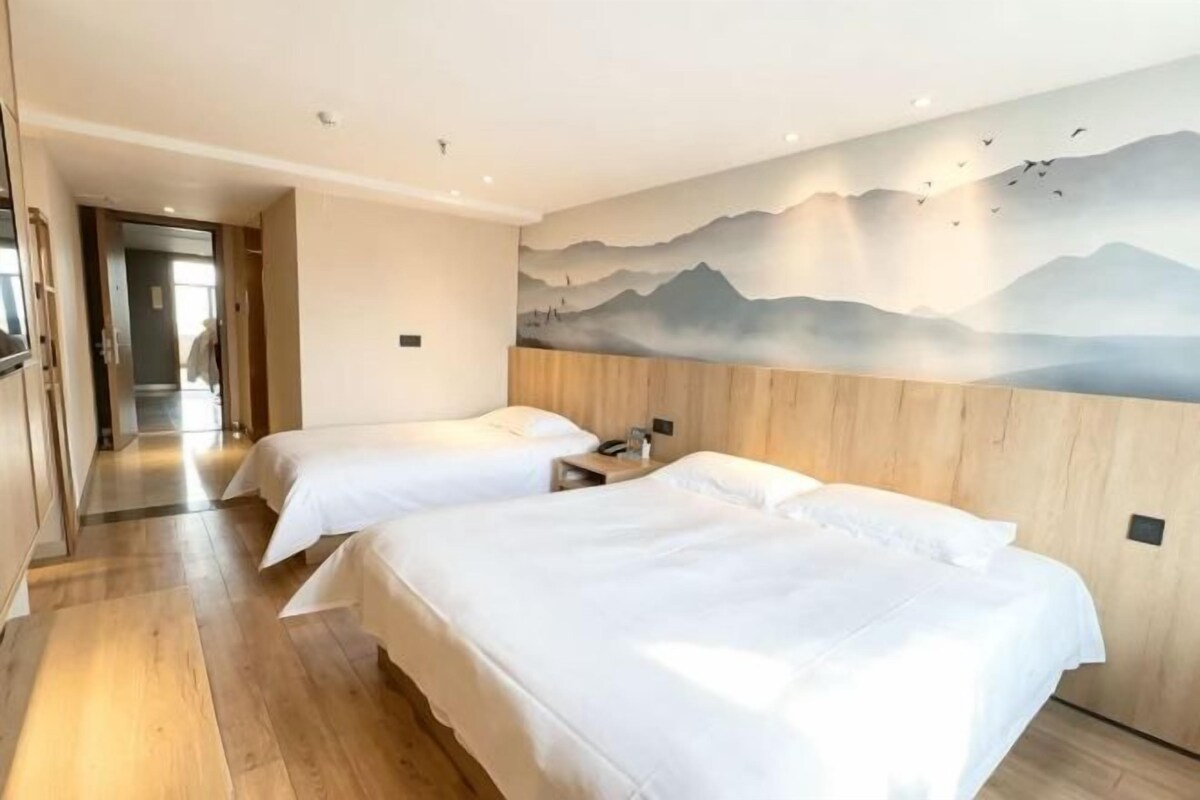 Habitación de hotel con dos camas, cabecero de madera, un cuadro de montañas y suelo de madera.