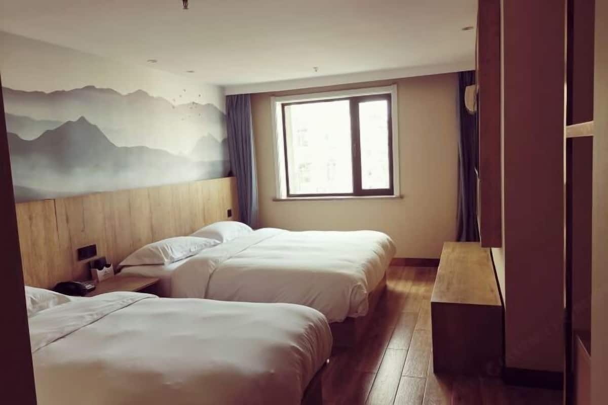 A hotel room with two beds, a wooden headboard, a large window with curtains, and a wall mural.