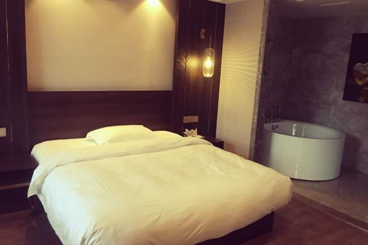 A hotel room with a bed, a wall-mounted light fixture, and a bathtub.