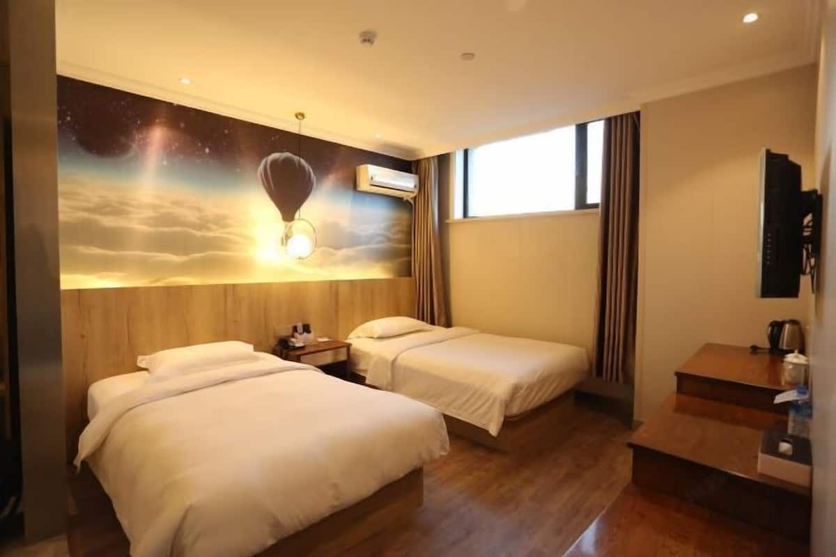 A hotel room with two beds, a wooden headboard, a mural of a hot air balloon, and a window with curtains.
